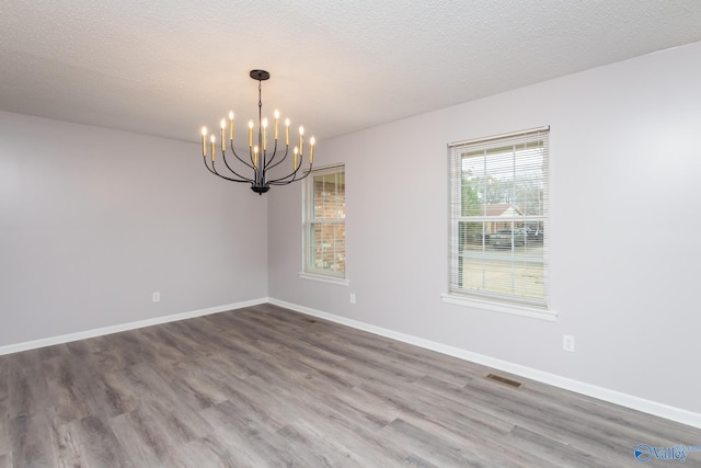 spare room featuring an inviting chandelier, hardwood / wood-style floors, and a textured ceiling