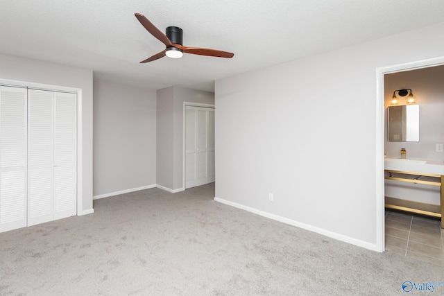 unfurnished bedroom featuring connected bathroom, ceiling fan, multiple closets, light carpet, and a textured ceiling