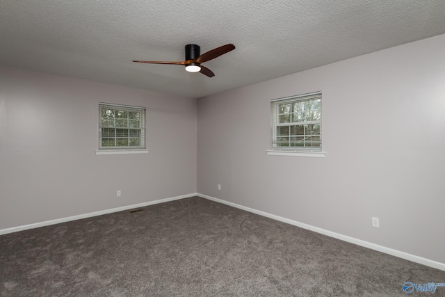 empty room with a wealth of natural light, a textured ceiling, and dark colored carpet