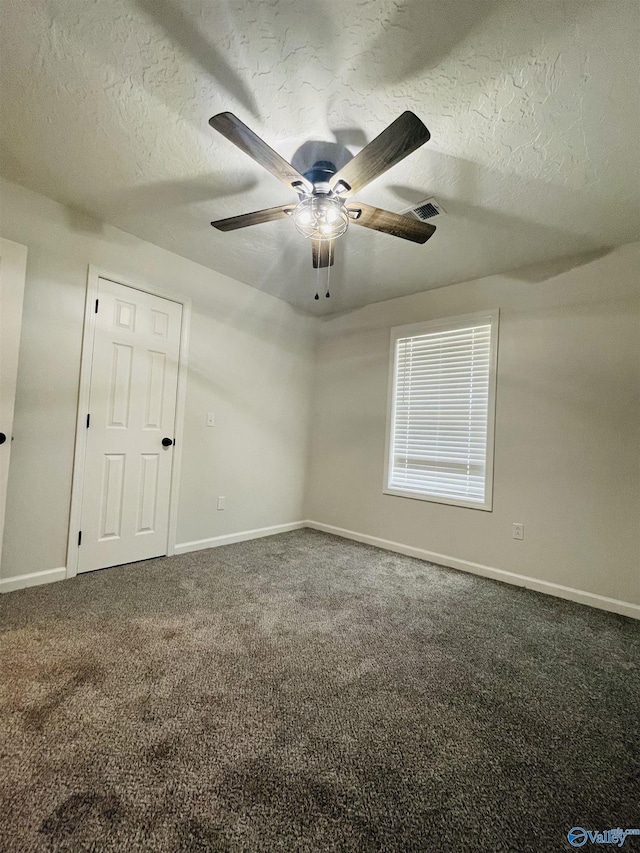 empty room featuring ceiling fan, dark carpet, and a textured ceiling