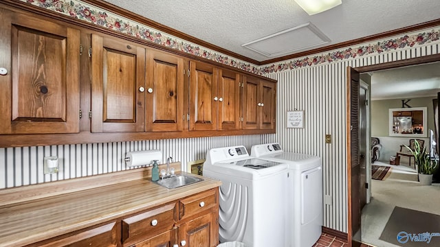 clothes washing area with sink, cabinets, ornamental molding, washing machine and dryer, and a textured ceiling