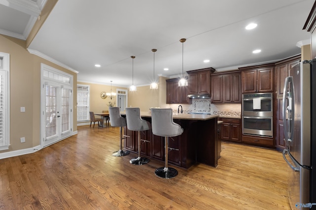 kitchen with a breakfast bar area, decorative backsplash, appliances with stainless steel finishes, ornamental molding, and light wood-type flooring