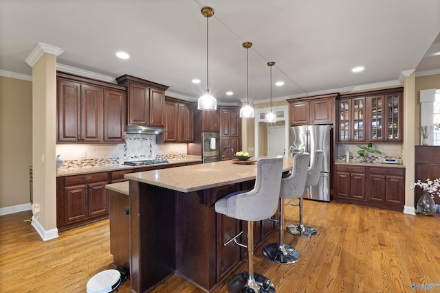 kitchen with stainless steel appliances, light wood-style floors, under cabinet range hood, and ornamental molding