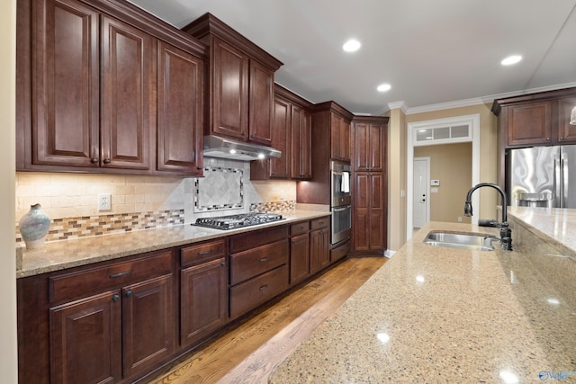 kitchen with ornamental molding, light stone countertops, stainless steel appliances, under cabinet range hood, and a sink