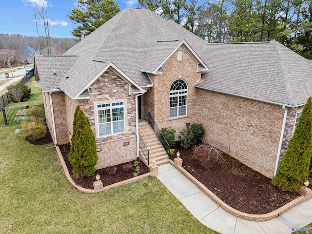 view of front of home featuring a shingled roof, a front lawn, fence, and brick siding