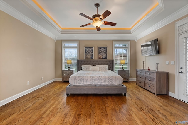 bedroom with a raised ceiling, multiple windows, and wood finished floors