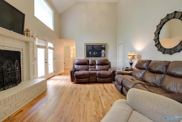 living room with baseboards, light wood-style flooring, a brick fireplace, and high vaulted ceiling