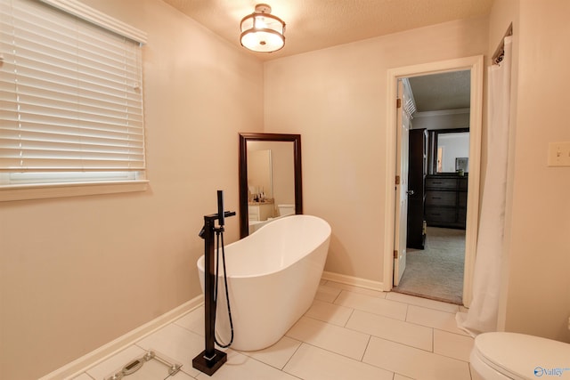 bathroom with toilet, baseboards, a textured ceiling, tile patterned floors, and a freestanding bath