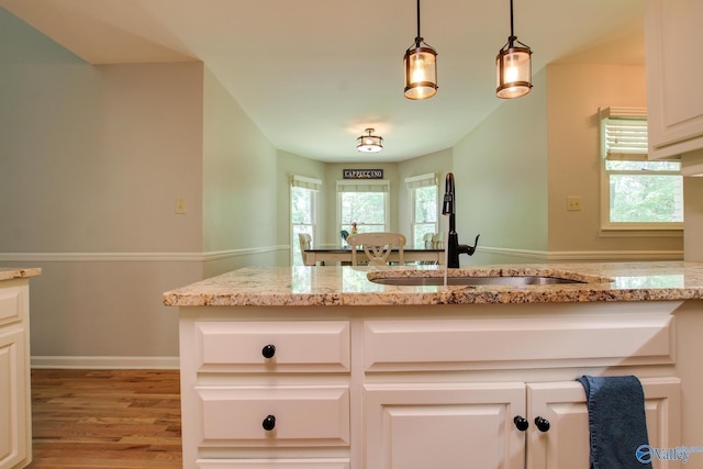 kitchen featuring light stone countertops, hanging light fixtures, a sink, and light wood finished floors