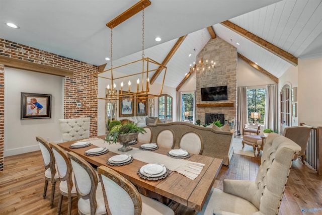 dining room with a chandelier, high vaulted ceiling, a stone fireplace, light wood-style floors, and beam ceiling