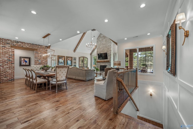 living room with light hardwood / wood-style floors, a chandelier, brick wall, lofted ceiling, and a stone fireplace