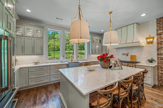 kitchen with hardwood / wood-style floors, backsplash, a kitchen island, sink, and hanging light fixtures