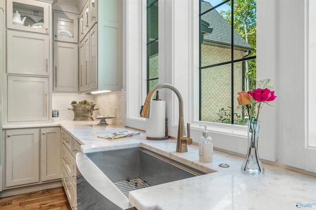 details with glass insert cabinets, a sink, backsplash, and light stone countertops