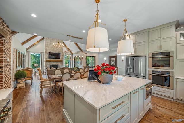 kitchen with a fireplace, stainless steel appliances, wood-type flooring, a center island, and vaulted ceiling with beams