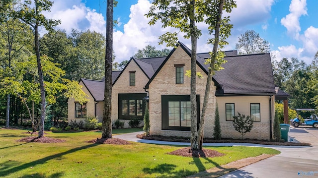 view of front of home featuring a shingled roof, a front yard, and brick siding