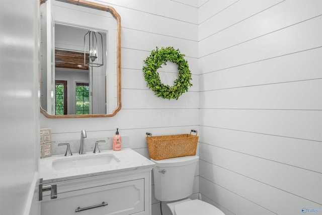 bathroom featuring toilet, wooden walls, and vanity