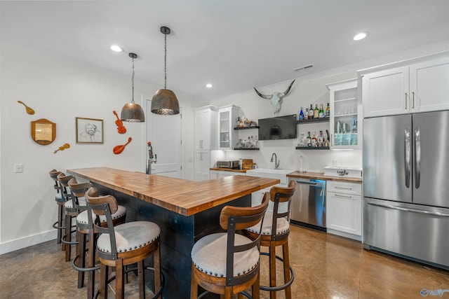 kitchen featuring white cabinets, a breakfast bar area, stainless steel appliances, and wooden counters