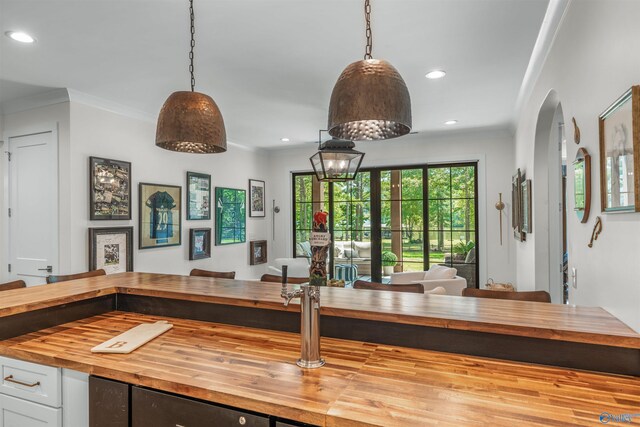 interior space featuring hanging light fixtures, white cabinetry, butcher block counters, and ornamental molding