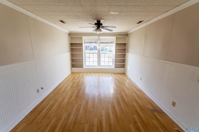 unfurnished room featuring ornamental molding, built in features, ceiling fan, and light hardwood / wood-style flooring