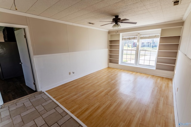 empty room featuring crown molding, wood-type flooring, built in features, and ceiling fan