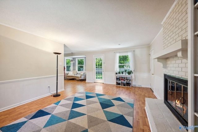 9410 Valley Ln, Huntsville, AL 35803 - living room featuring wood finished floors, a brick fireplace, a textured ceiling, ornamental molding, and wainscoting