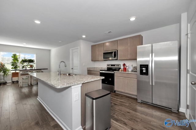 kitchen with sink, dark hardwood / wood-style floors, an island with sink, appliances with stainless steel finishes, and light stone counters