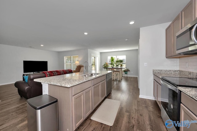 kitchen with light stone countertops, appliances with stainless steel finishes, dark wood-type flooring, sink, and an island with sink