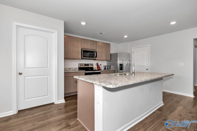 kitchen with appliances with stainless steel finishes, dark hardwood / wood-style floors, tasteful backsplash, and an island with sink