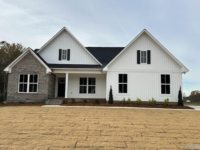 modern inspired farmhouse with covered porch, brick siding, board and batten siding, and a shingled roof