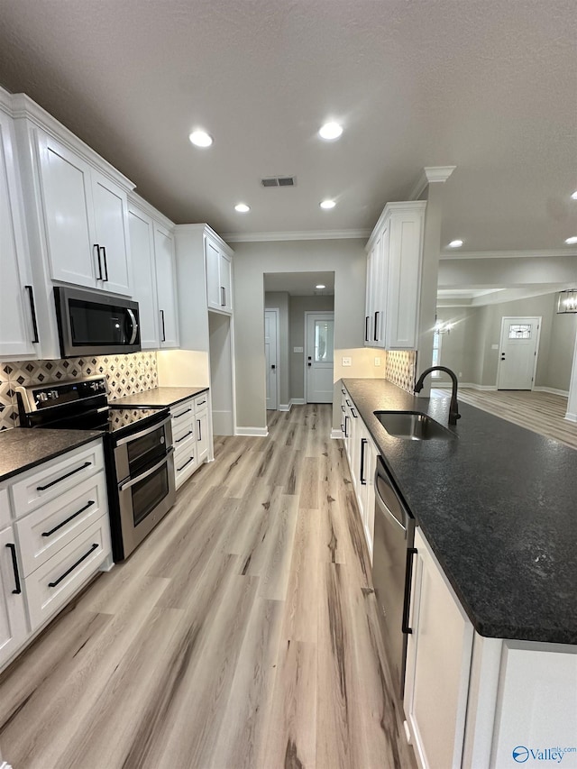 kitchen with appliances with stainless steel finishes, white cabinetry, a sink, and tasteful backsplash