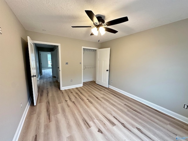 unfurnished bedroom with a textured ceiling, ceiling fan, light wood-style floors, baseboards, and a closet