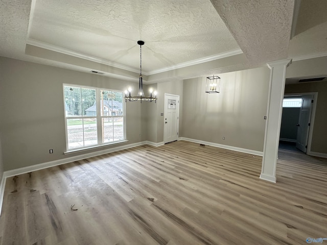 unfurnished dining area featuring a textured ceiling, wood finished floors, visible vents, a tray ceiling, and ornate columns