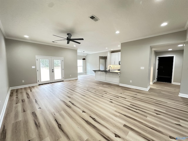 unfurnished living room featuring light wood finished floors, french doors, a sink, and baseboards