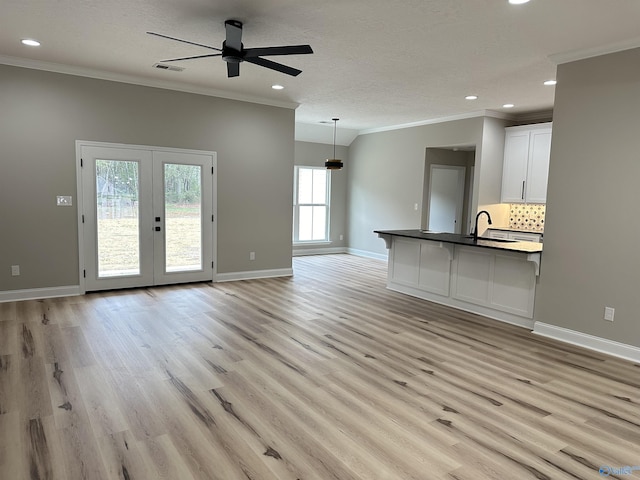 unfurnished living room featuring a textured ceiling, baseboards, light wood-style floors, french doors, and ornamental molding