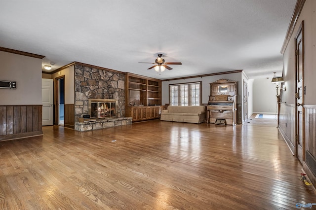 unfurnished living room with ceiling fan, light hardwood / wood-style flooring, a stone fireplace, and built in features