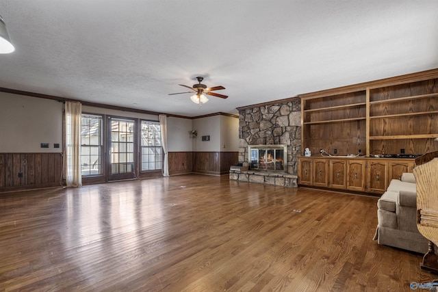 unfurnished living room with ceiling fan, ornamental molding, hardwood / wood-style flooring, built in shelves, and a stone fireplace