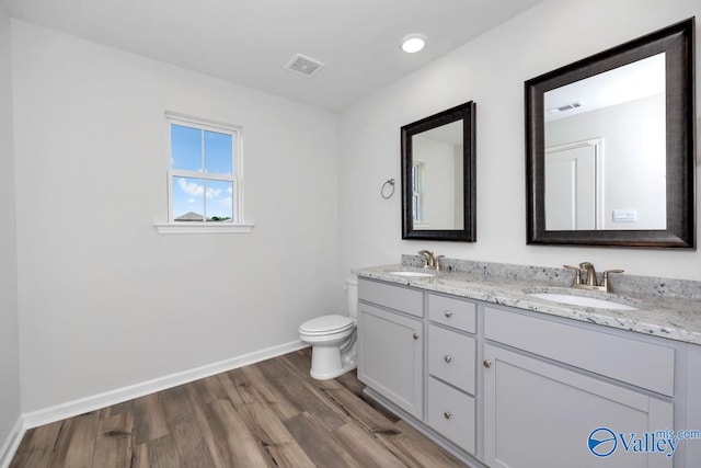 bathroom with dual vanity, toilet, and wood-type flooring