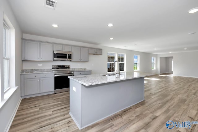 kitchen featuring an island with sink, light hardwood / wood-style floors, range with electric cooktop, sink, and gray cabinetry