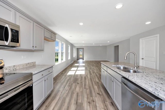 kitchen featuring gray cabinets, light wood-type flooring, sink, light stone countertops, and appliances with stainless steel finishes