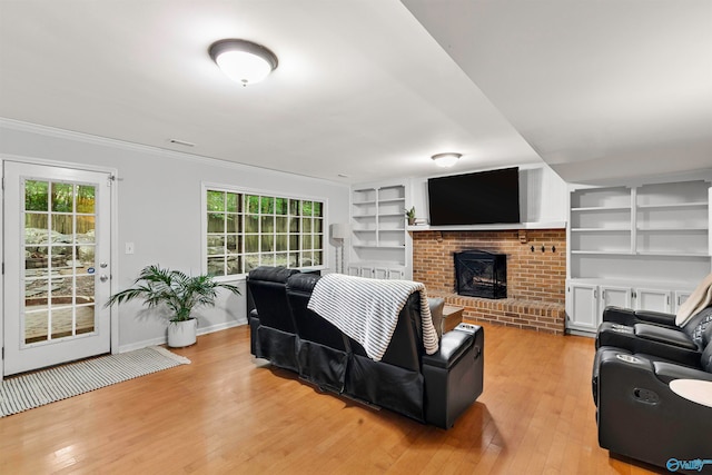 living room featuring light hardwood / wood-style flooring, ornamental molding, built in features, and a brick fireplace