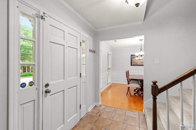 tiled entrance foyer with ornamental molding, a healthy amount of sunlight, and a chandelier