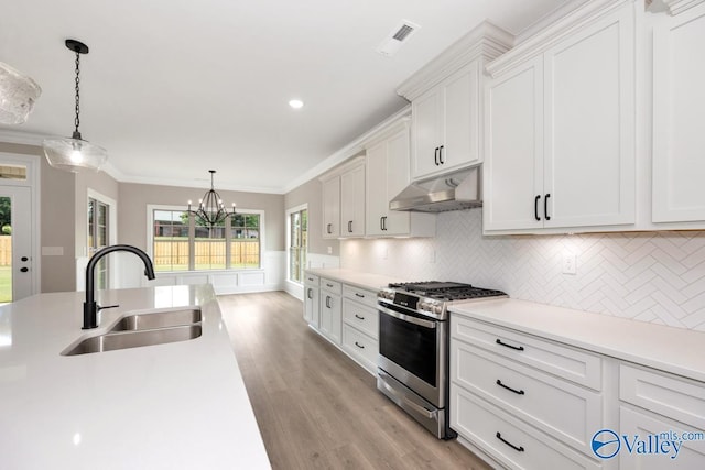 kitchen featuring sink, stainless steel gas stove, crown molding, decorative light fixtures, and white cabinets