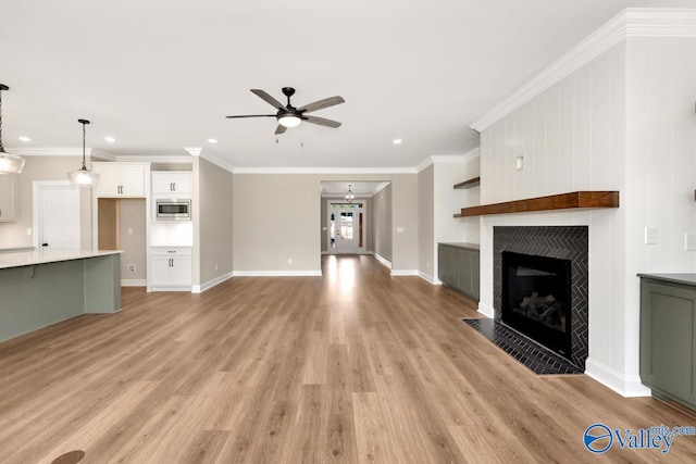 unfurnished living room featuring a fireplace, ornamental molding, ceiling fan, and light wood-type flooring