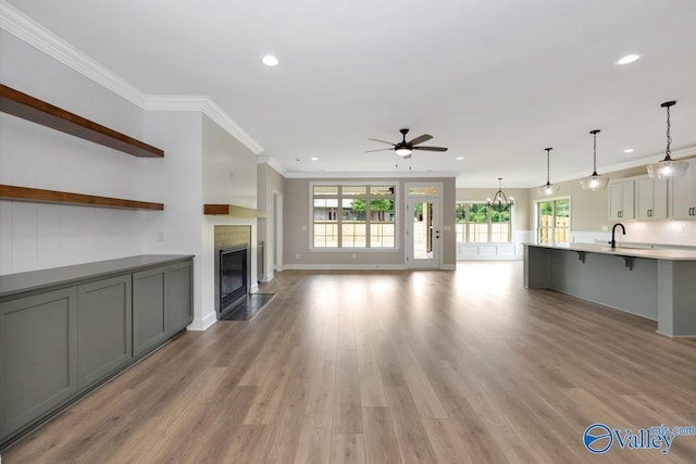 unfurnished living room with ornamental molding, sink, ceiling fan with notable chandelier, and light wood-type flooring