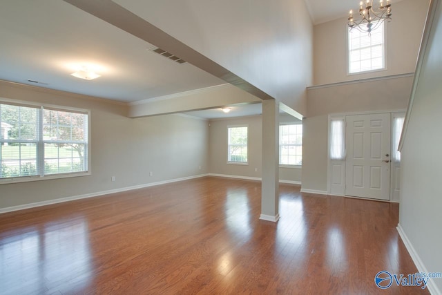 entrance foyer with ornamental molding, a towering ceiling, hardwood / wood-style floors, and a notable chandelier