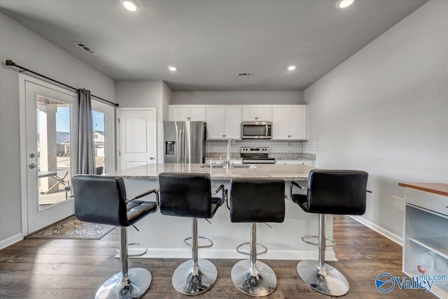 kitchen with sink, stainless steel appliances, light stone counters, white cabinets, and decorative backsplash