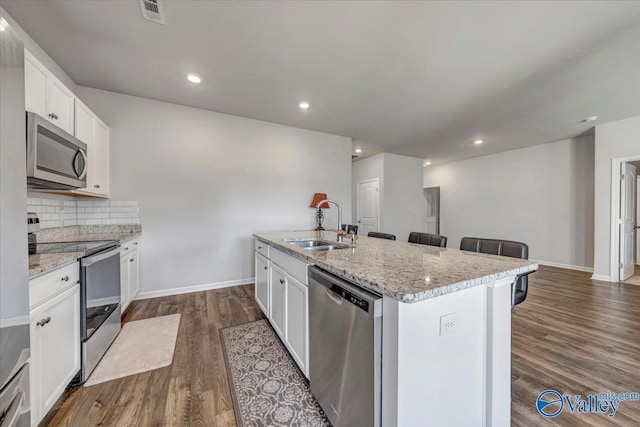 kitchen with appliances with stainless steel finishes, sink, white cabinets, dark hardwood / wood-style flooring, and a kitchen island with sink