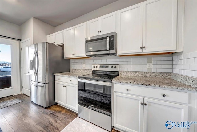 kitchen featuring dark wood-type flooring, white cabinetry, appliances with stainless steel finishes, light stone countertops, and decorative backsplash