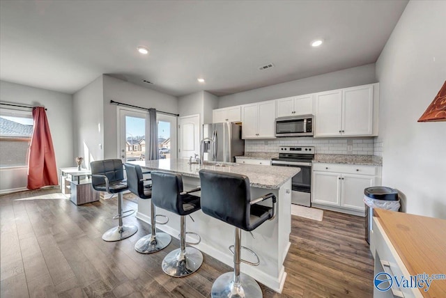 kitchen with appliances with stainless steel finishes, a kitchen island with sink, light stone counters, tasteful backsplash, and white cabinets