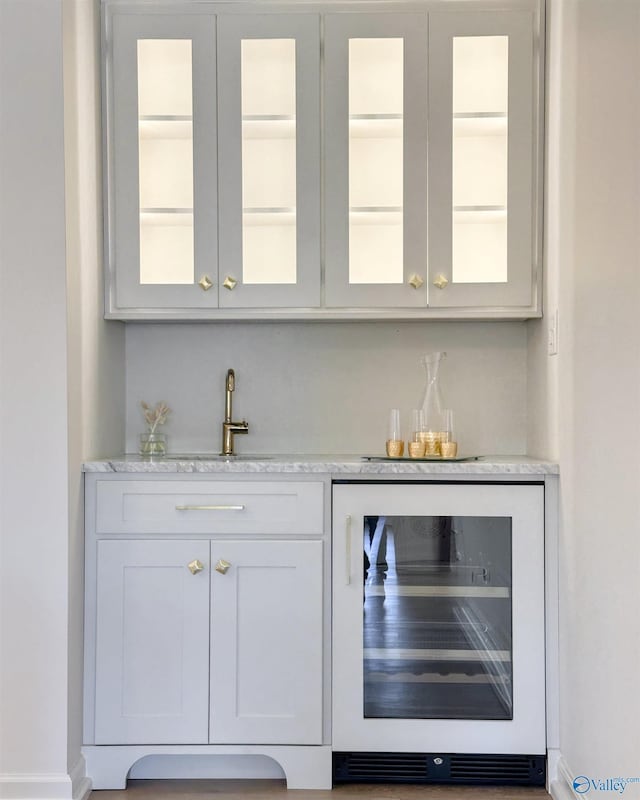bar with white cabinetry, sink, wine cooler, and light stone counters